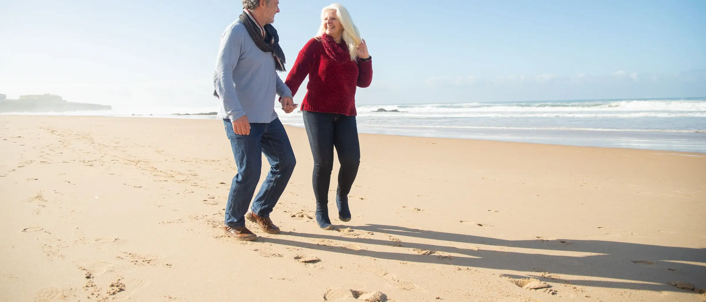 Pareja adulta caminando de la mano por la playa al atardecer